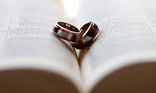 Zwei Eheringe formen ein Herz auf einem aufgeschlagenen Buch.