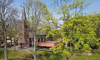 Backsteinkirche mit Turm, umgeben von Bäumen im Frühling.