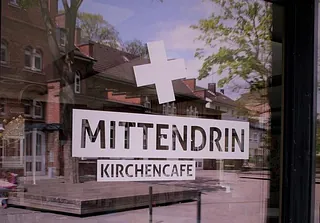 Schild im Schaufenster „MITTENDRIN KIRCHENCAFÉ“.