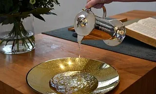 Silberne Kanne gießt Wasser in eine goldene Schale auf einem Holztisch.