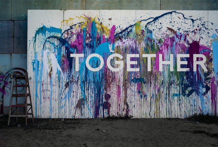 Graffiti „TOGETHER“ auf einer mit Farbspritzern bemalten Wand.