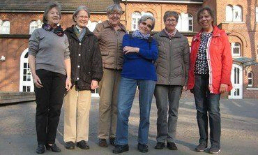 Sechs Frauen posieren für ein Gruppenfoto vor einem Backsteingebäude.