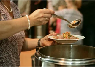 Eine Person schöpft Essen aus einem Topf.