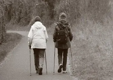 Zwei Personen mit Wanderstöcken gehen auf einem Weg (Schwarzweiß).