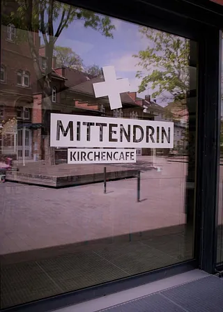 Ein Schild an einem Fenster mit der Aufschrift „MITTENDRIN KIRCHENCAFÉ“.