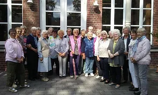 Eine Gruppe älterer Menschen posiert für ein Foto vor einem Gebäude.