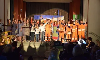 Kinder und Erwachsene stehen jubelnd auf einer Bühne.