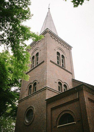 Kirchturm aus Stein, von unten gesehen, umgeben von Bäumen.